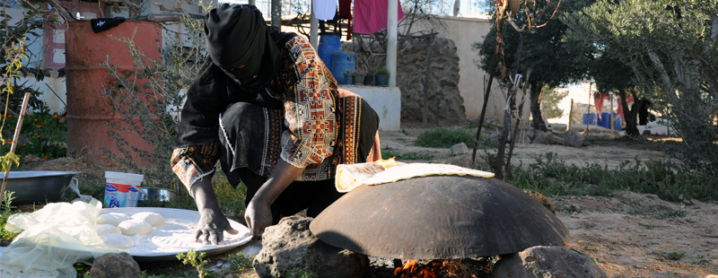 Main image: A local woman prepares fresh dough while baking bread over a fire in front of her home near Umm el-Jimal's ruins.